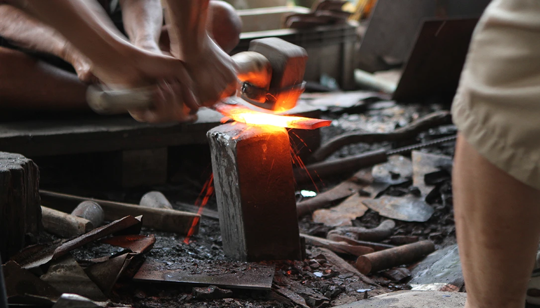 Sparks fly as a Thai bladesmith hammers red-hot steel on a bamboo-handled anvil in the village of Aranyik.