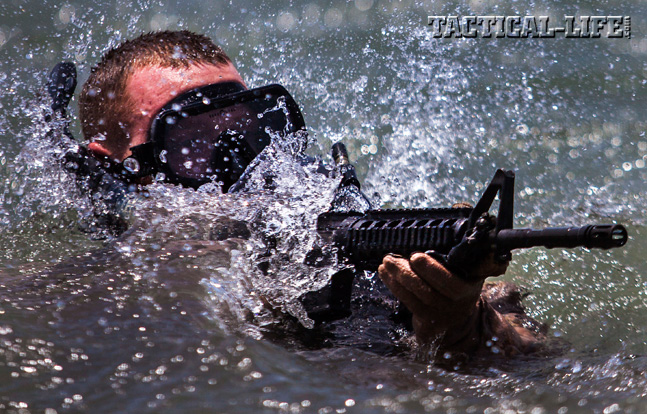 A Marine assigned to the 26th Marine Expeditionary Unit Maritime Raid Force emerges from the surf armed with a Colt M4 Carbine.
