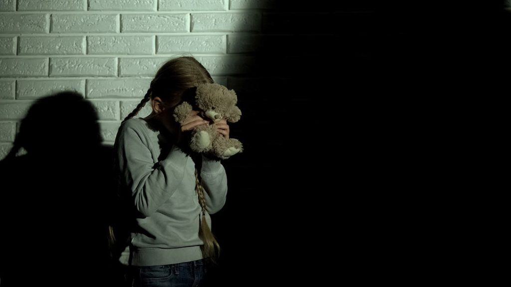 A young girl hides her face with a teddy bear.