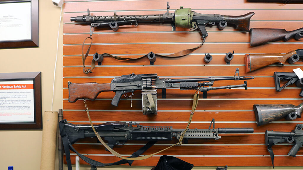 The left wall of the shop is stacked with belt-fed machineguns.
