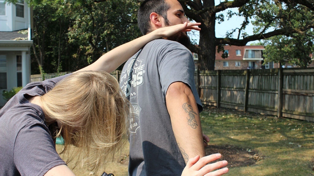 The girl pulls her head out while keeping control of the attacker’s arm.