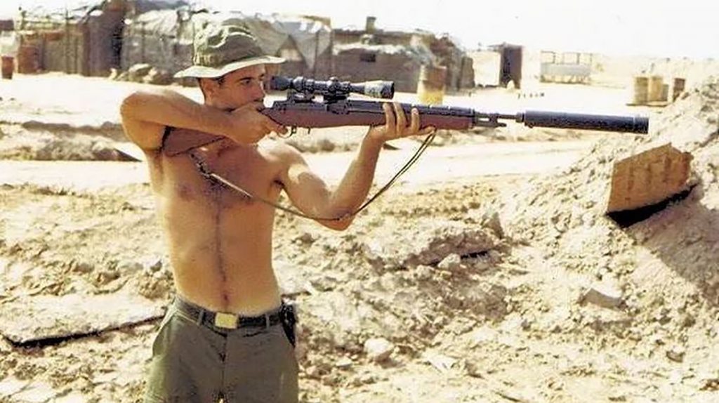 Carlos poses in Vietnam with a scoped bolt-action rifle.
